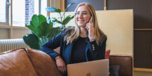 woman talking on the phone sitting on a couch with her laptop